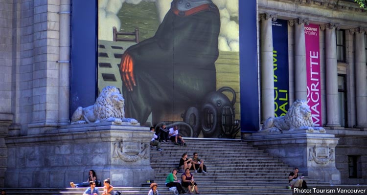 People sit on the steps of the Vancouver Art Gallery, between two lion statues.