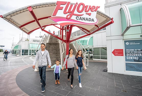 A family walks from a set of stairs below a FlyOver Canada sign.