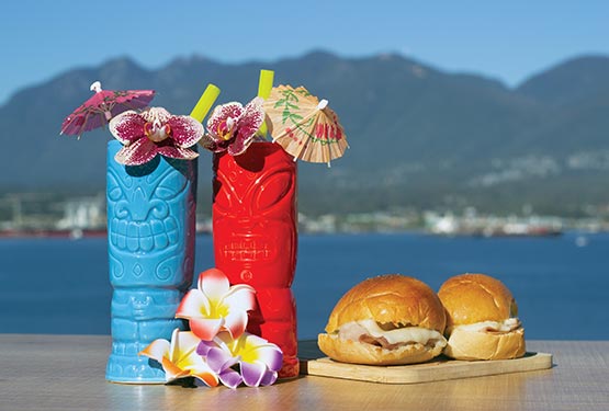 Two colourful tiki cups sit next to two slider burgers