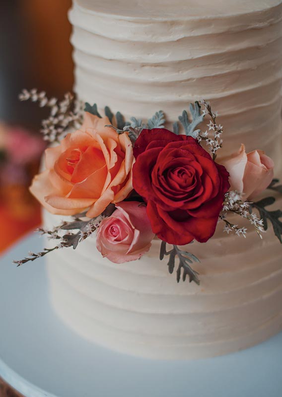 A wedding cake decorated with red and pink roses.