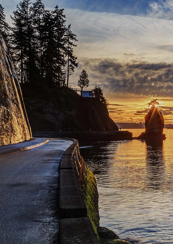 A pathway along a seashore with the sun setting below clouds.