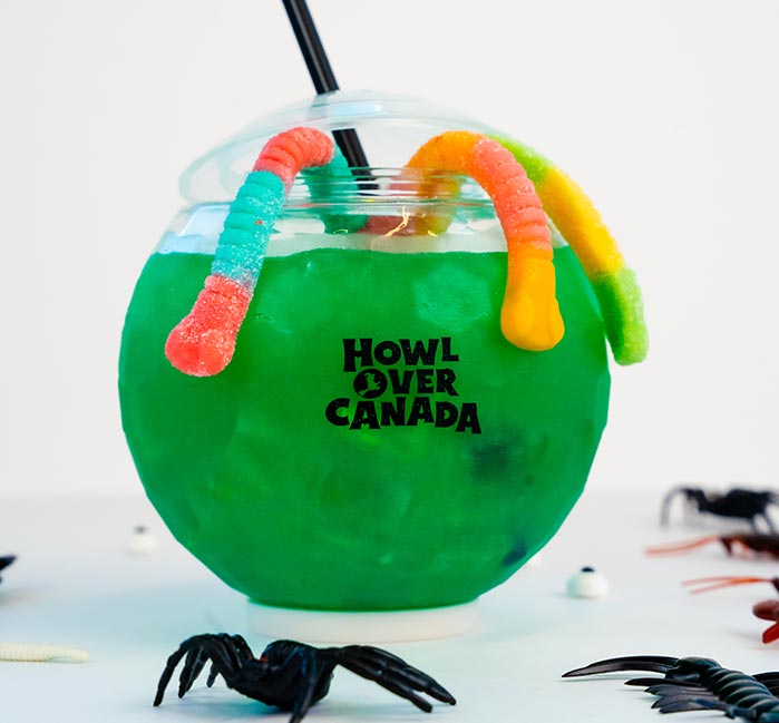 A green drink with gummy worms in a spherical cup.