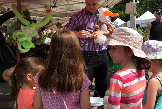A balloon artists makes animals for a group of children outside.