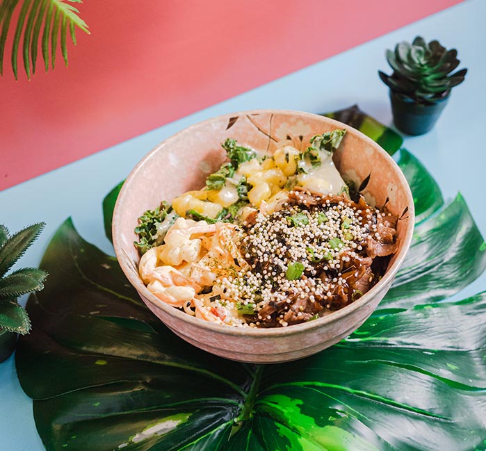 A bowl of poke sits on a large green leaf on a table.