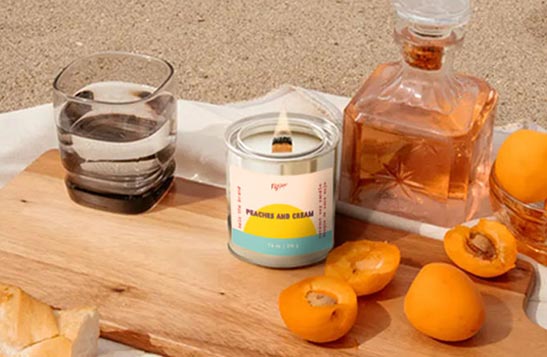 A Mala the Brand candle sits on a white table with fruit around it.