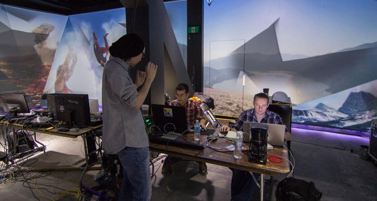 The Moment Factory Team works on the UpLift experience at a desk of computers and other digital equipment