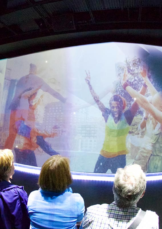 A crowd watches the UpLift experience with dancers on screen.