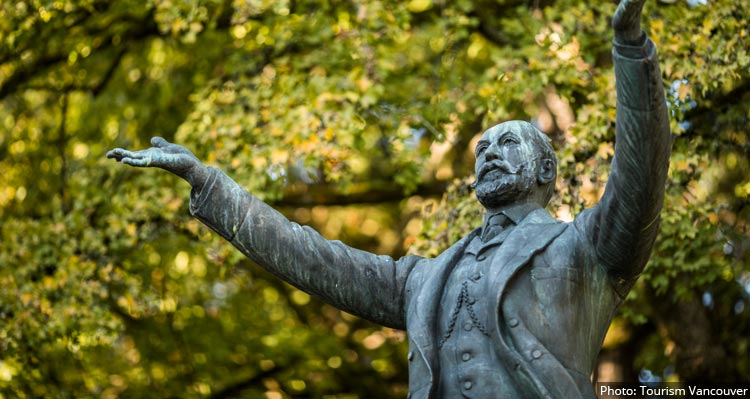 A statue of Lord Stanley with arms raised among leafy trees.