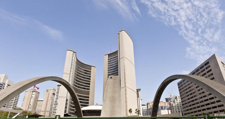 Two towers circle around a white domed building, behind arches.