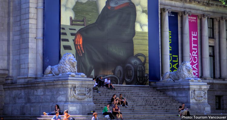 People sit on the steps of the Vancouver Art Gallery, between two lion statues.