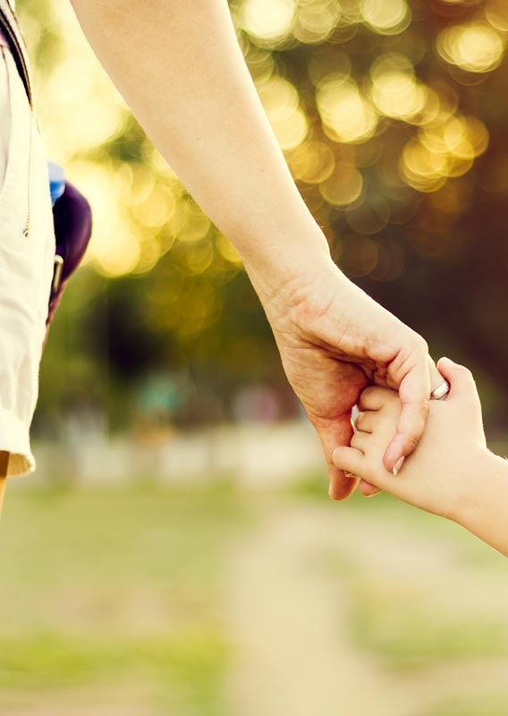 A mother and daughter hold hands in a park.