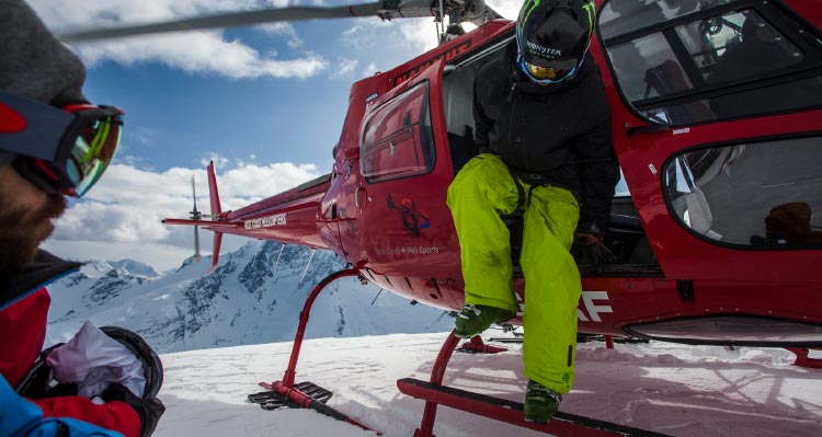 A skiier gets out of a red helicopter.