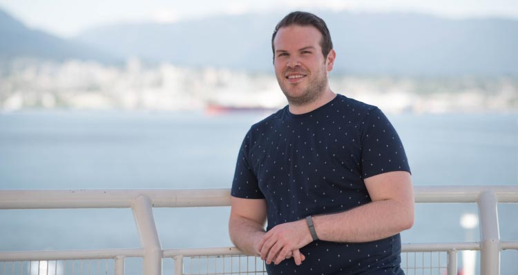 A man leans against a white railing next to the sea.