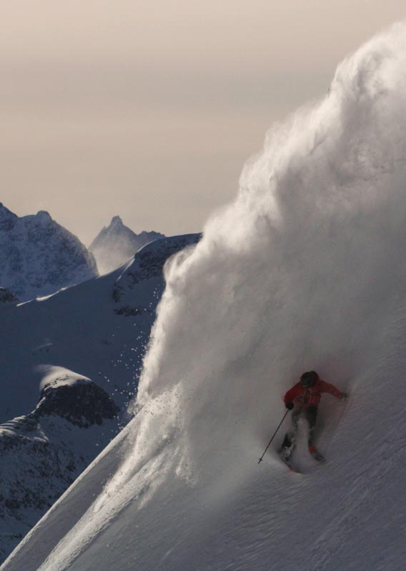 A skiier makes a plume of snow powder on a mountainside.
