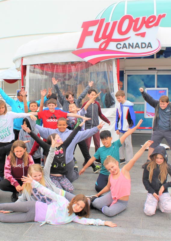 A group of kids pose for a photo out front of the FlyOver Canada building