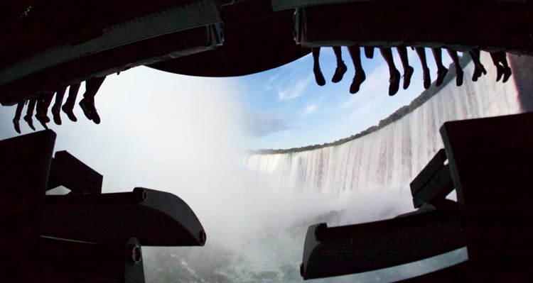 Visitors' feet dangle from the FlyOver Canada flight-ride, while Niagara Falls is shown on the screen.