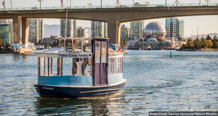 A small blue boat moving along water near a tall bridge with skyscrapers behind.
