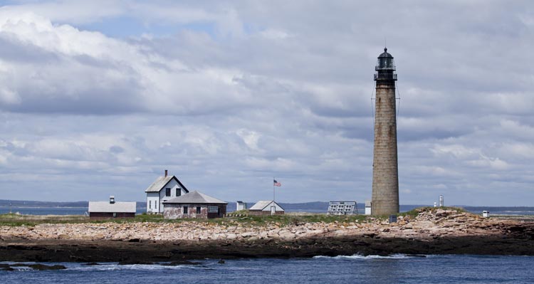 An historic lighthouse stands a the seashore near some buildings.