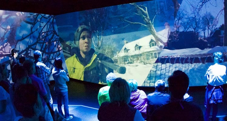 A group of people watch a cinematic presentation showing Canadian life.