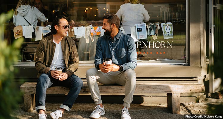 Two friends sit on a bench outside a cafe