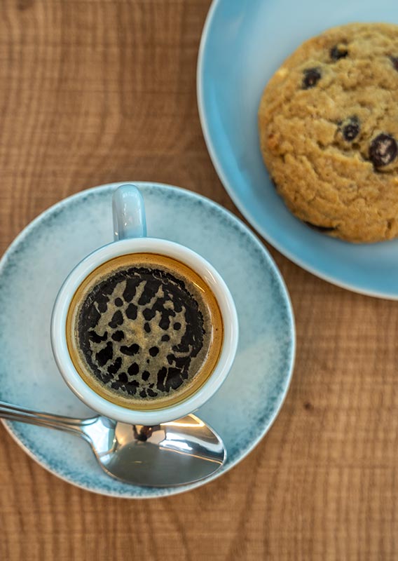 An espresso and cookie on separate plates on a wooden table.