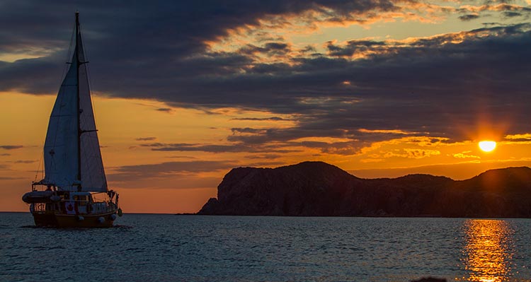 A sailboat on the ocean with an orange sky.