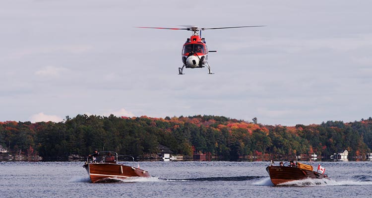 A helicopter flies over a lake near some small boats.
