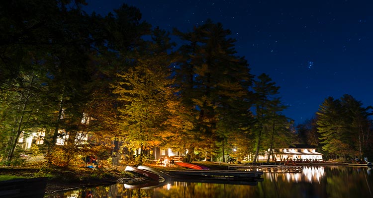 Some cottages lit up at night alongside a calm lake.
