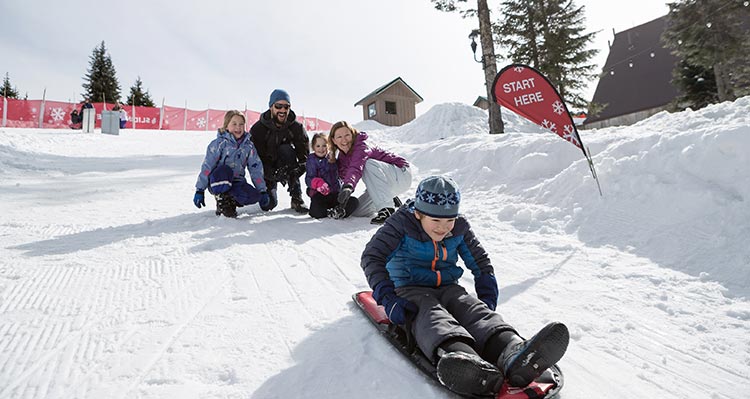 A family on a snowy hill tobagganing.