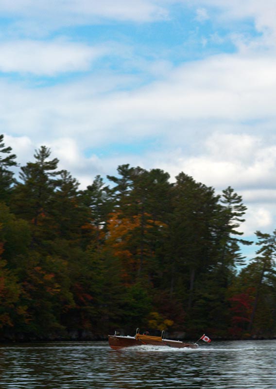 Some small boats on the water near trees with autumn colours.