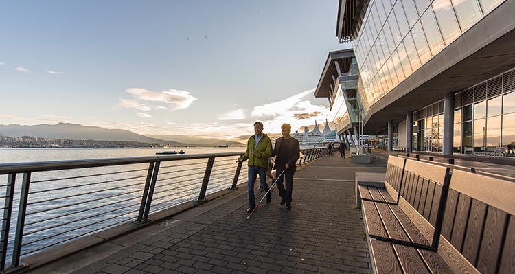 Two people walk along a pathway next to an open harbour.