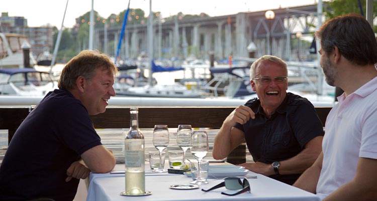 Three people sit at a dock side dinner table.