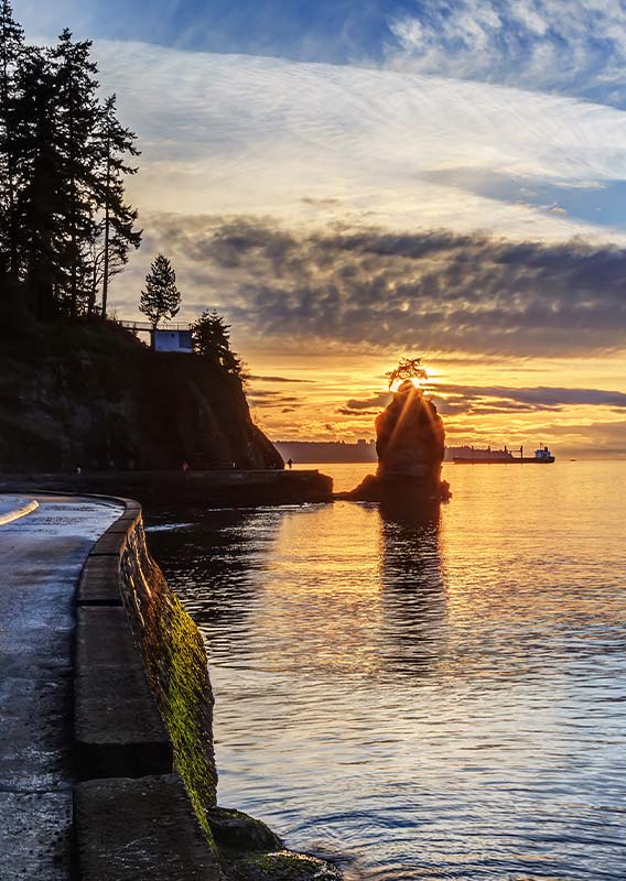 A lighthouse at sunset with hills behind ocean water.