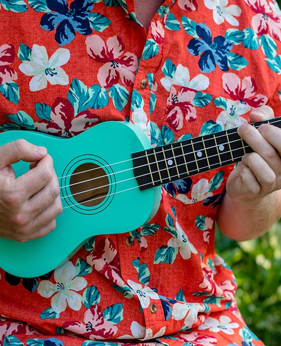 A man wearing a bright floral shirt strums a ukulele.