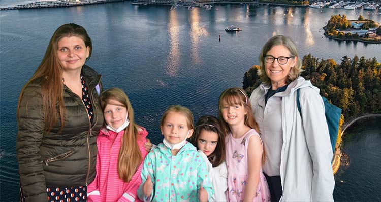 Two women and 4 young girls pose in front of the FlyOver Canada Vancouver flight background.